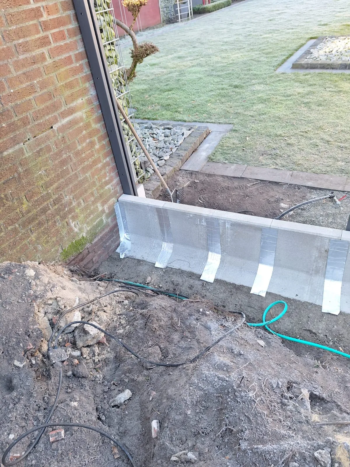 Sicht auf die vorbereitete Fundamentkante für die Terrasse mit Kabeln und Erde im Vordergrund