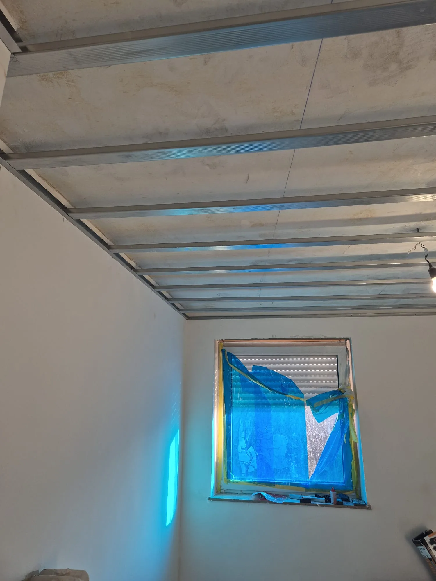 Deckenverkleidung im Zimmer mit einem Fenster und blauer Folie