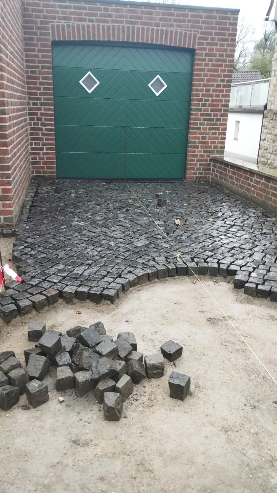 Pflasterarbeiten mit schwarzen Steinen in einer Garageneinfahrt