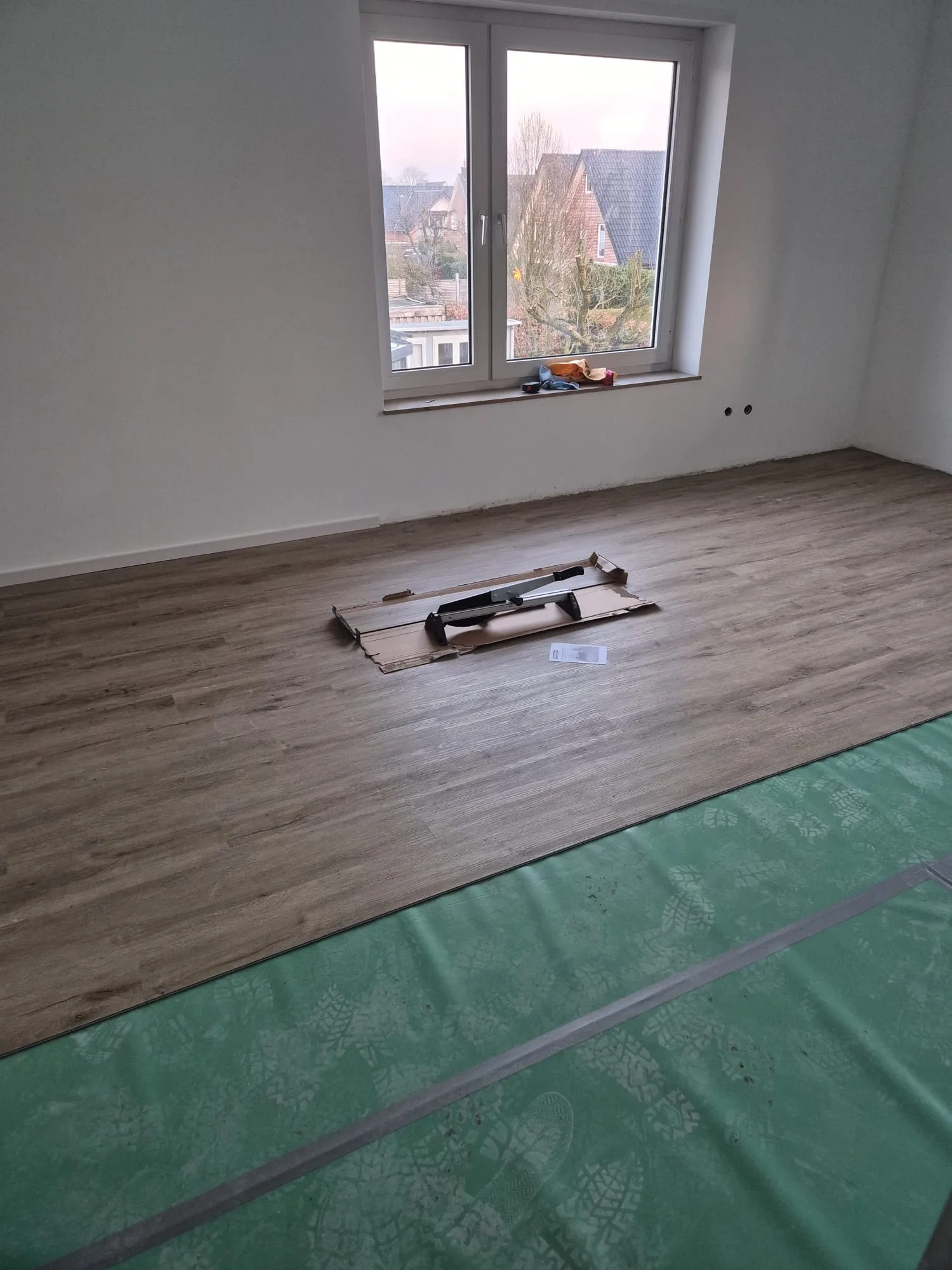Laminatboden wird verlegt, mit Ausschnitt für eine Wandöffnung und grünem Estrich-Schutz